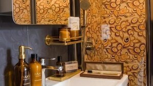 A bathroom with a white sink, gold-patterned walls, a mirror, and toiletries. - Luna Hotel & Terrace (Baku)