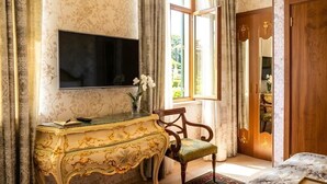 A room with a TV mounted on the wall, a wooden cabinet with a green cushioned chair, and a wooden door with a mirror. - Luna Hotel & Terrace (Baku)