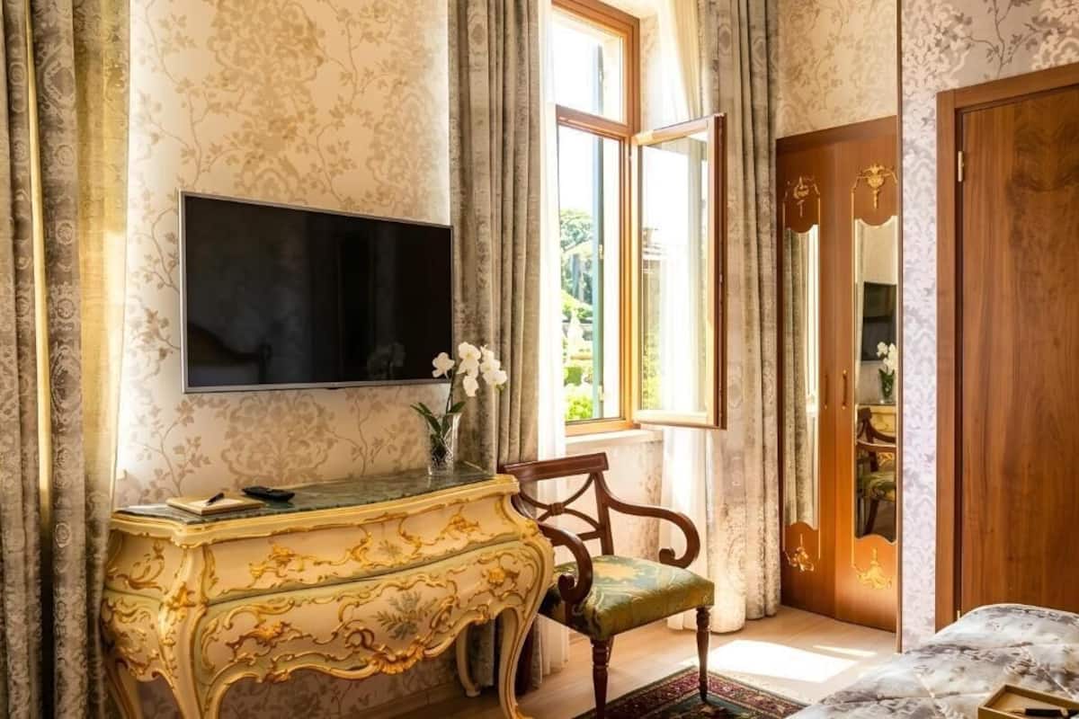 Habitació amb televisió penjada a la paret, un armari de fusta i una cadira amb coixí verd, més una porta de fusta amb mirall.