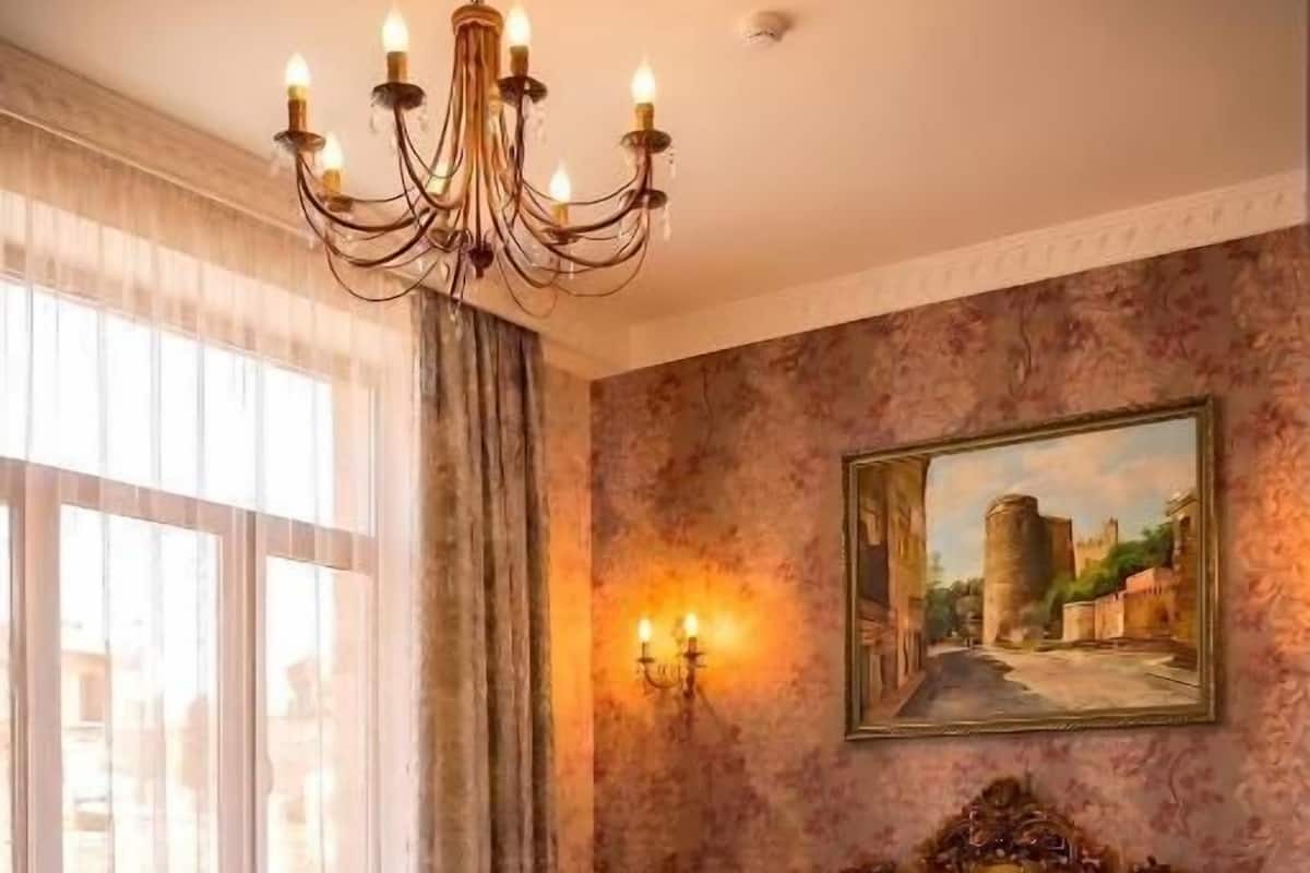 A bedroom with a large bed, a chandelier, a painting, and a view of the city through the window.