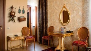 A room with a wooden door, a small table with a glass top, two chairs with red cushions, a mirror with a gold frame, and a patterned wall. - Luna Hotel & Terrace (Baku)