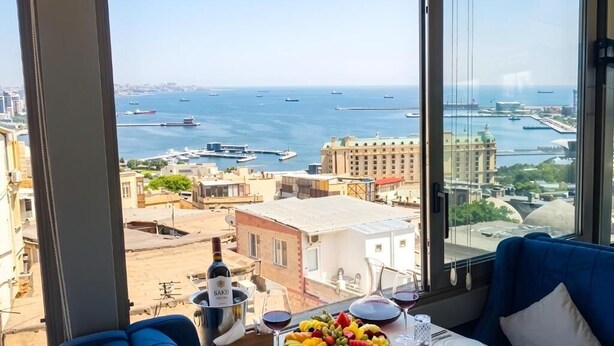 A dining table with a fruit platter, wine glasses, and a bottle of Baku wine, overlooking a marina with boats and buildings. - Luna Hotel & Terrace (Baku)