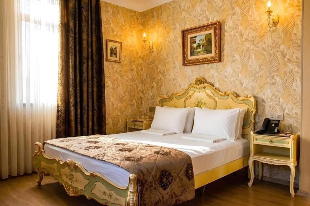 Una habitació d'hotel amb un llit gran, una tauleta de nit, una làmpada i un quadre al mur.