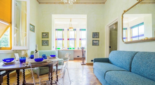 Un comedor con mesa de madera, sillas y tazones azules. Hay un sofá azul y un espejo en la pared.