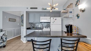 A kitchen with grey cabinets, a central island, a microwave, a refrigerator, and a coffee maker. - Ocean Forest Plaza 912 (Myrtle Beach)