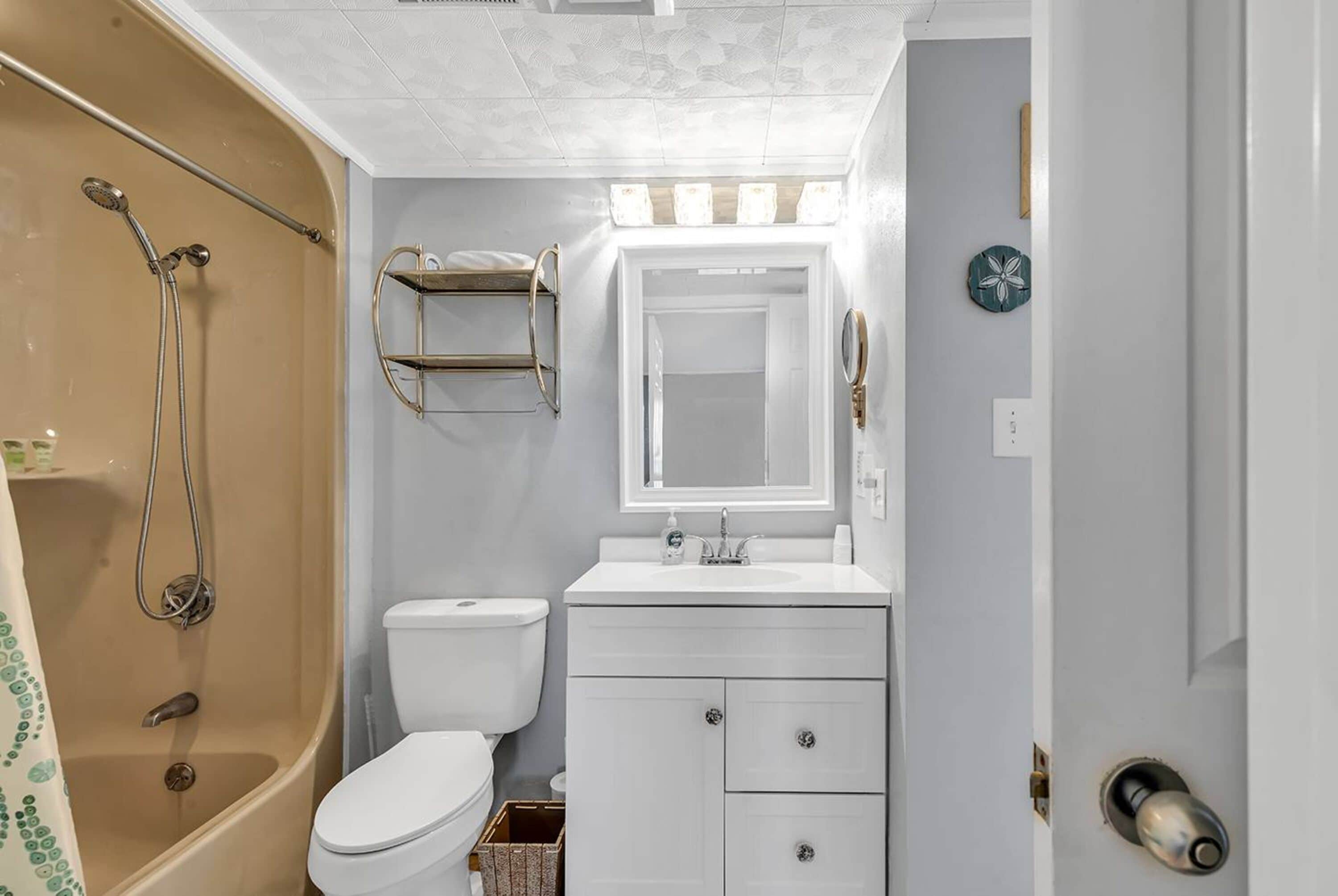 Een badkamer met douche, toilet, wastafel en spiegel.