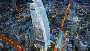 Un edificio moderno de gran altura con fachada curva, rodeado de un entorno urbano denso con calles y otros edificios a la vista.