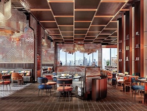 A modern restaurant interior with a city view, wooden flooring, and a variety of seating arrangements.