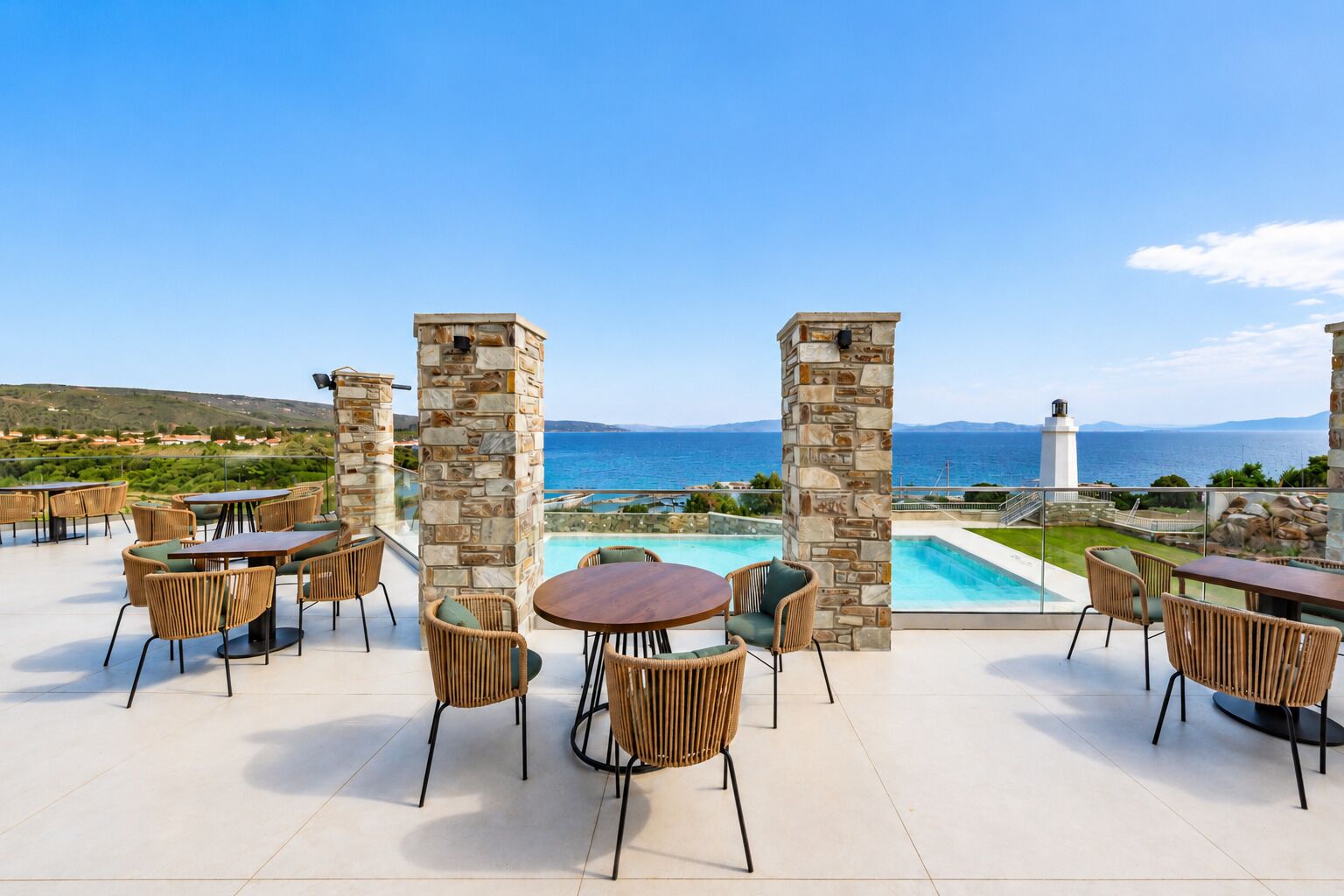 Une terrasse extérieure dotée de piliers en pierre, de meubles en osier et offrant une vue sur la mer et un phare.