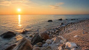 Ein Strand mit Kieselsteinen und Felsen, ruhigem Wasser und einem Sonnenuntergang.
