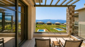 Ein Balkon mit Blick auf ein Schwimmbecken und Häuser, eine Steinsäule und eine Glastür.