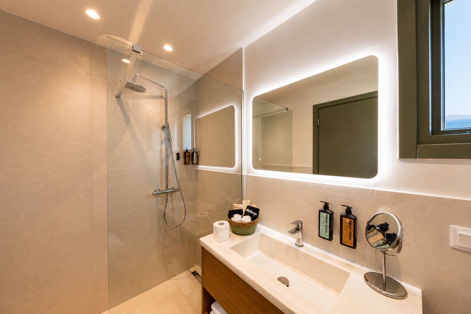 A modern bathroom with a glass-enclosed shower, a vanity with a mirror, and toiletries.