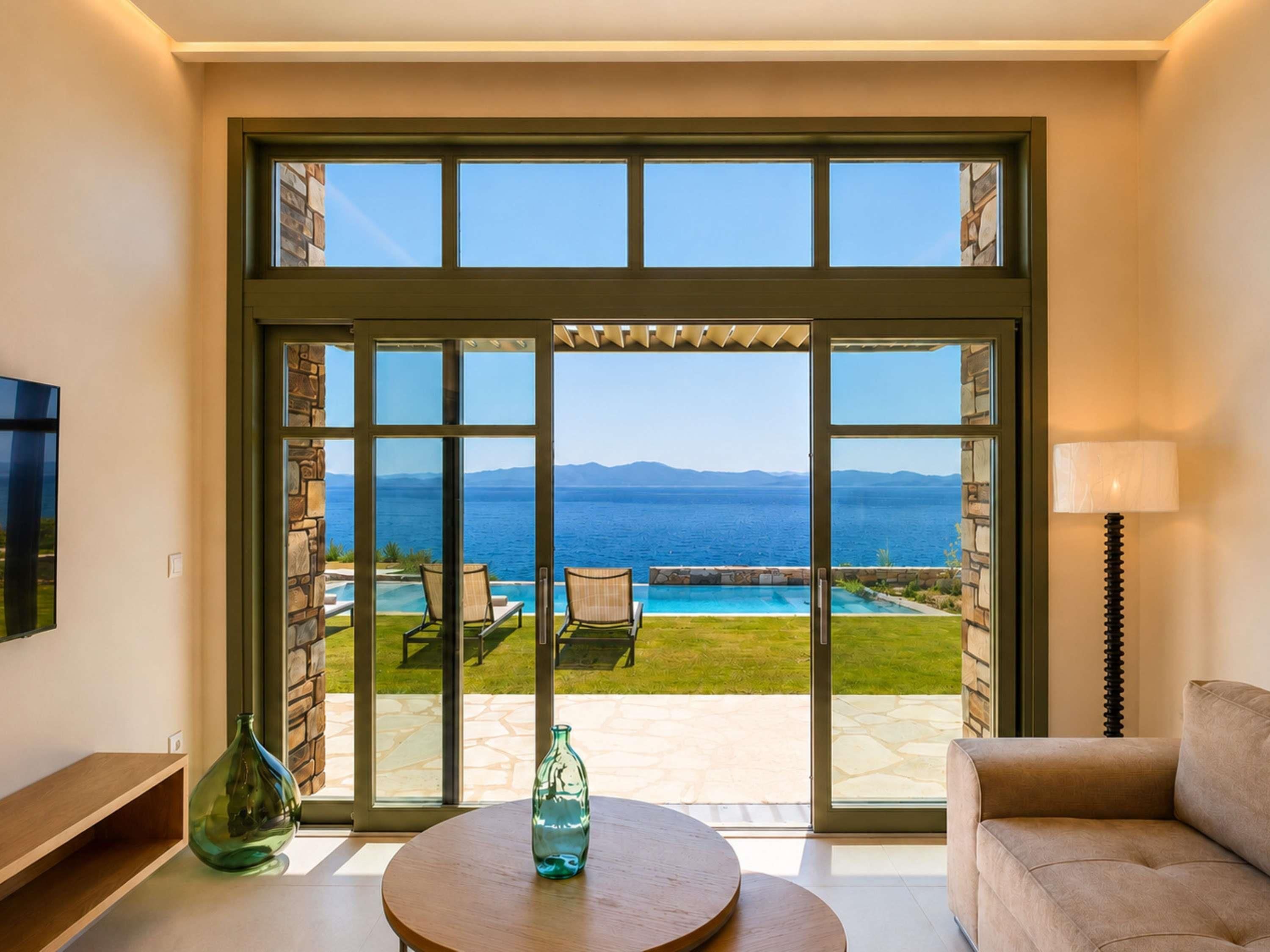 A room with a large sliding glass door leading to an outdoor pool area with a view of the sea and mountains.