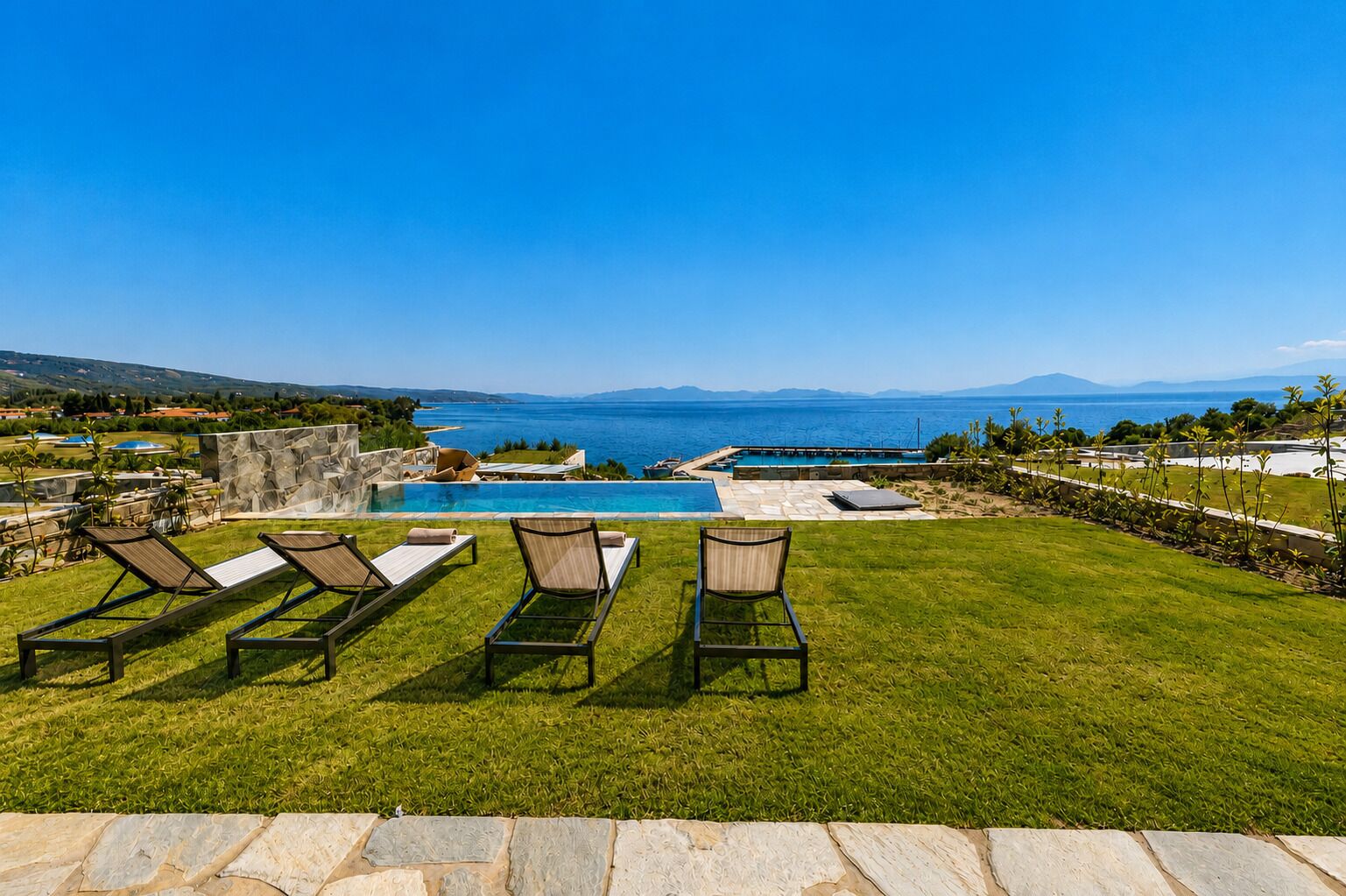 Ein Poolbereich mit Liegestühlen, einer Steinmauer und Blick aufs Meer.