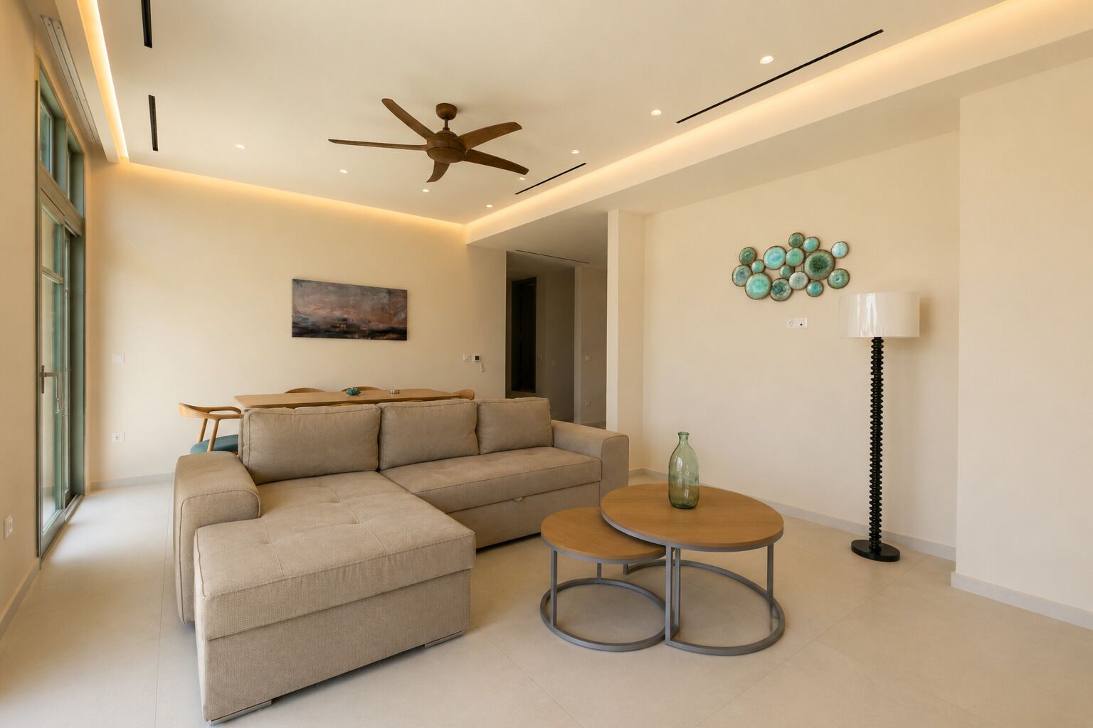 A modern living room with a sectional sofa, a round coffee table, a ceiling fan, and a wall-mounted light fixture.