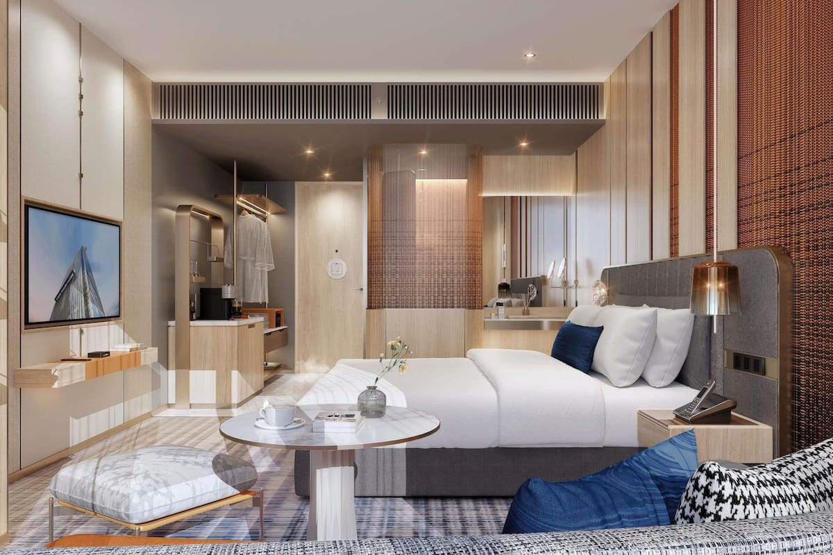 A modern hotel room with a bed, bedside table, lamp, and a TV mounted on the wall.