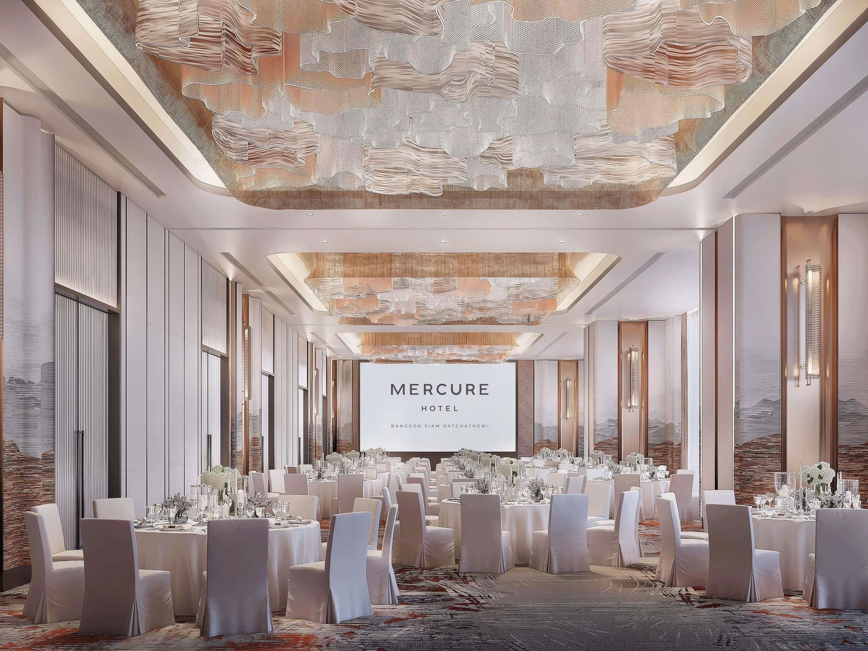 A spacious conference room with a large screen displaying 'MERCURE HOTEL' and a modern ceiling design.