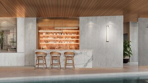 Una zona de bar con mostrador de mármol, sillas de madera y estantes llenos de botellas.