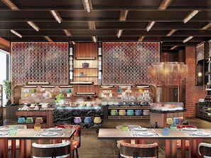 A restaurant with a high ceiling, exposed beams, and a central island with a chef. Tables are set with plates and cutlery. - Mercure Bangkok Siam Ratchathewi (Bangkok)