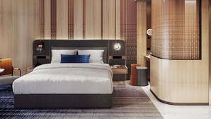 Una habitación de hotel moderna con una cama grande, una mesita de noche, una tocador empotrado con espejo y un reloj de pared.