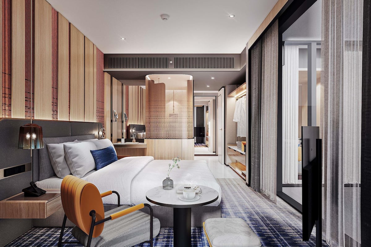 A modern hotel room with a bed, a small table, a chair, and a television.