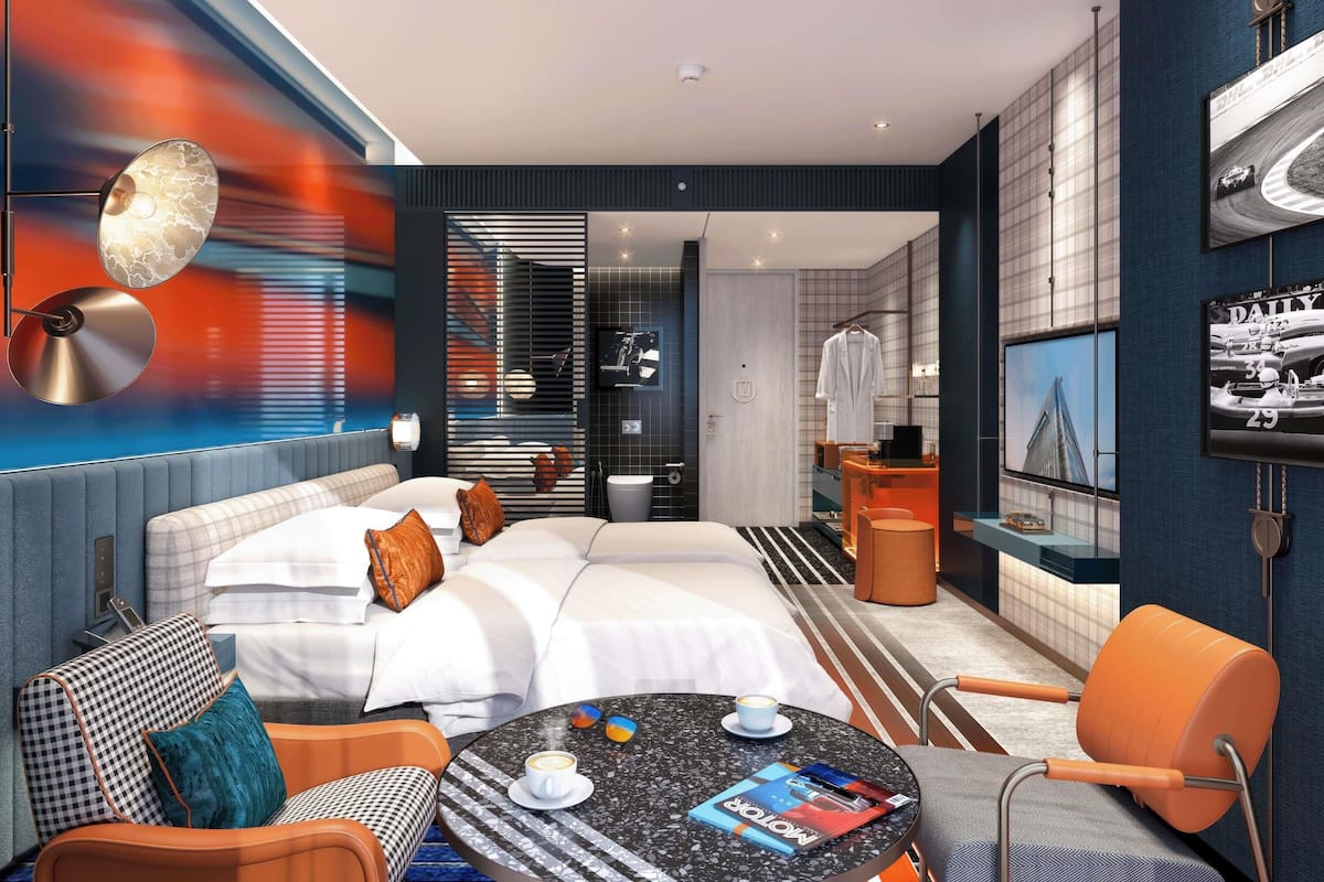 A modern hotel room with a large bed, a round table with a magazine, a coffee cup, and a TV on the wall.