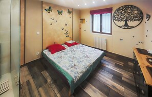 A bedroom with a bed, a radiator, a window with a curtain, and wall decorations including butterflies and a tree. - Confortable Appartement (Servian)