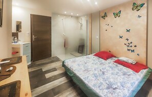 A bedroom with a bed, a shower, a wooden dresser, and a mirror. - Confortable Appartement (Servian)