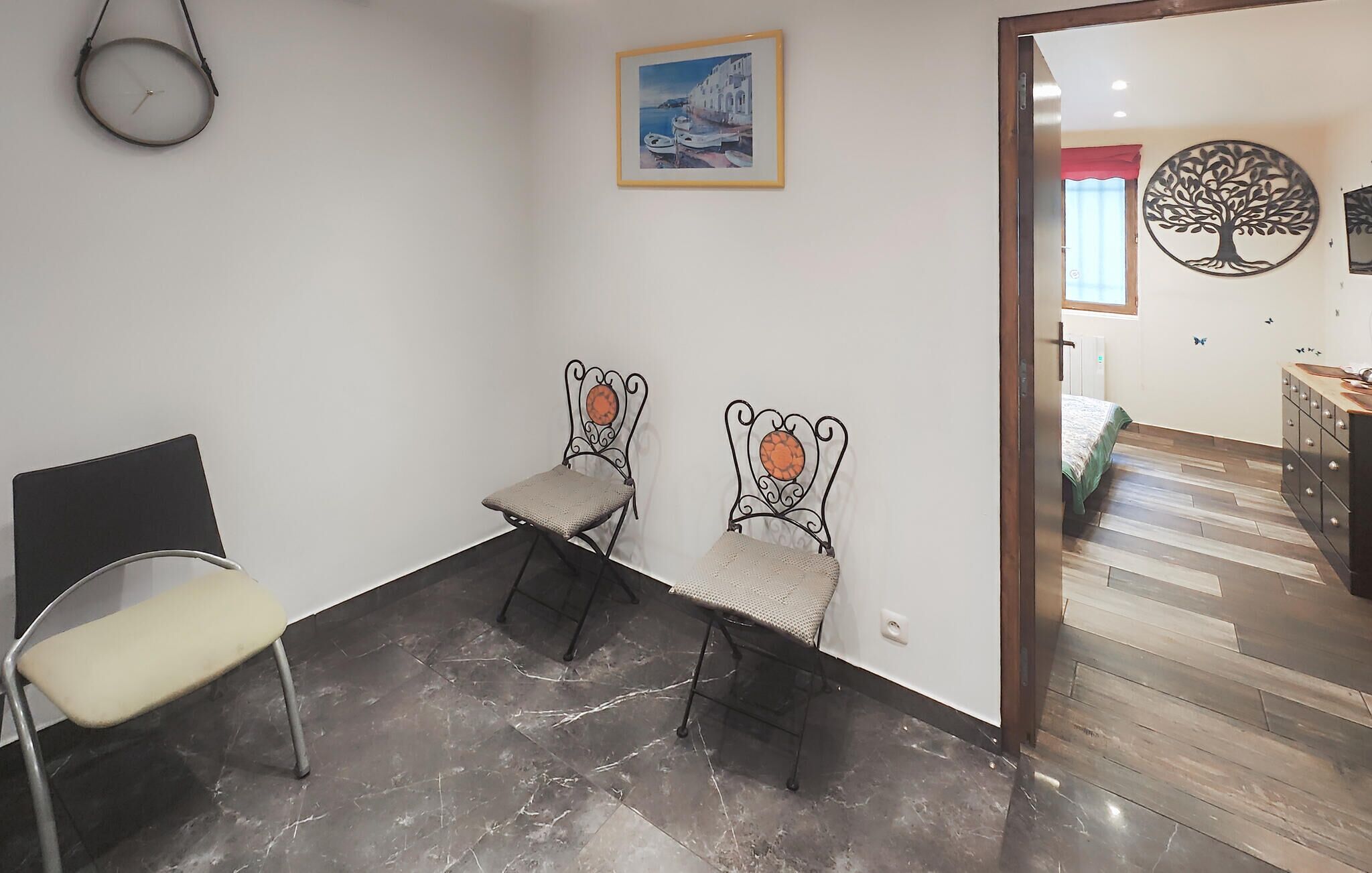 A room with a marble floor, two metal chairs with cushions, a clock on the wall, and a framed painting.