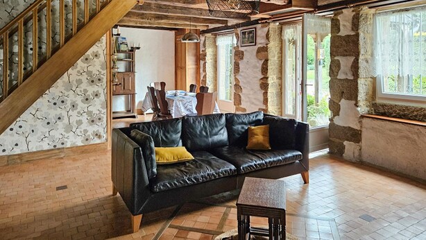 Ein rustikales Interieur mit freiliegenden Steinwänden, einer schwarzen Ledersofa, einer Holztreppe und einem Essbereich.