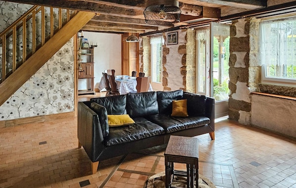 Ein rustikales Interieur mit freiliegenden Steinwänden, einer schwarzen Ledersofa, einer Holztreppe und einem Essbereich.