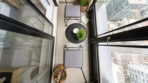 Ein Balkon mit zwei Stühlen, einem kleinen Tisch, einem Blumentopf und Blick auf die Stadt.