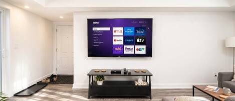 Ein modernes Wohnzimmer mit einem an der Wand befestigten Flachbildfernseher, einem schwarzen Konsolentisch und einem grauen Sofa.