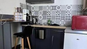 Et lille køkken med en sort bordplade, et hvidt køleskab, en rød mikrobølgeovn og en mønstret bagplade.
