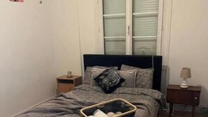 Een slaapkamer met een bed, nachtkastje, lamp, raam met zonwering en een decoratie aan de muur.