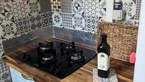 Een keuken met een gasfornuis, een decoratieve spatwand en lichtblauwe kastjes.