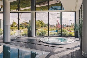 Ein moderner, überdachter Poolbereich mit großen Glaswänden, einem Whirlpool und Liegestühlen.