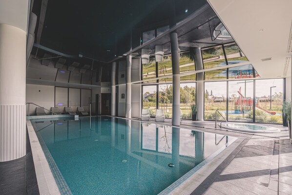 Ein Innenpool mit großen Glaswänden, Blick auf einen Spielplatz und einem modernen architektonischen Design.