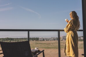Eine Person in einem gestreiften Bademantel steht an einem Fenster mit Blick auf ein Feld und Gebäude.