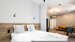 Una camera d'albergo moderna con un muro a motivi geometrici, una testiera in legno, un letto con lenzuola bianche, un piccolo comodino, un condizionatore d'aria a parete e un'area salotto con divano e poltrone.