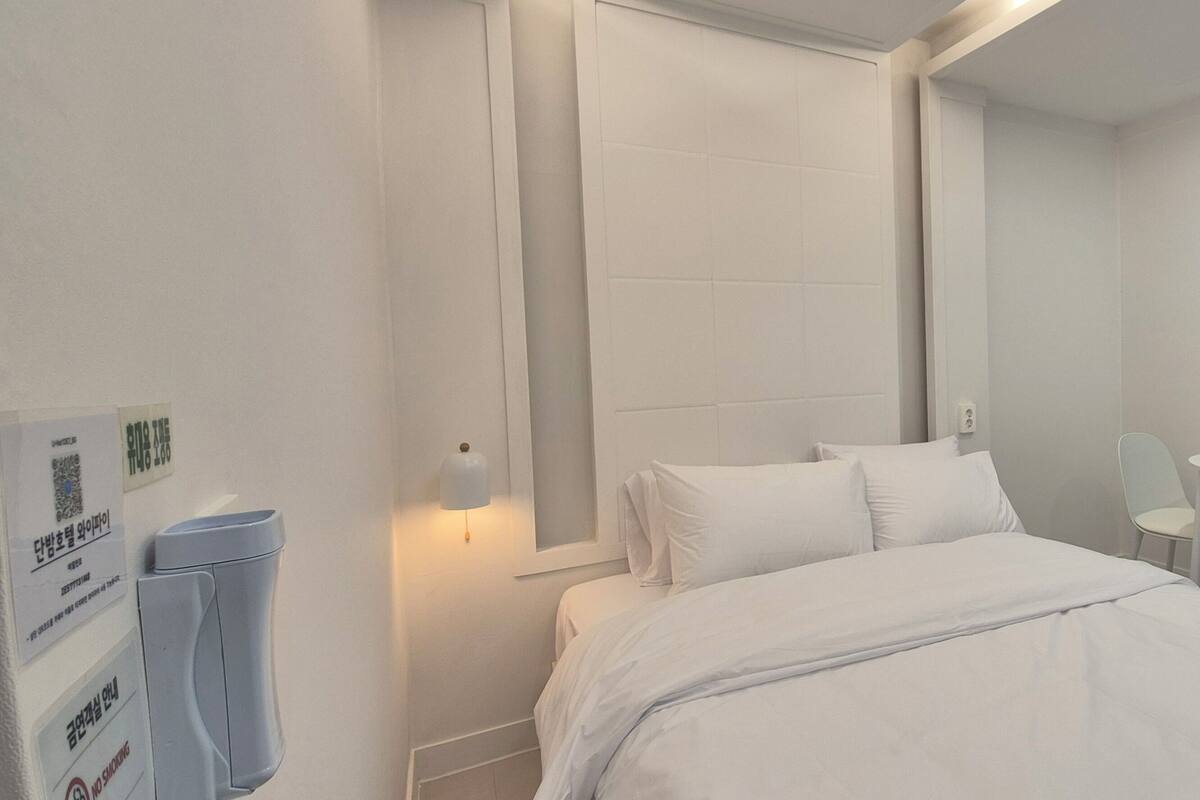Habitación de hotel con cama, una mesita, dos sillas, una ventana con cortinas y un purificador de aire instalado en la pared.