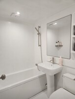 Un baño moderno con bañera, lavamanos pedestal, inodoro y espejo.