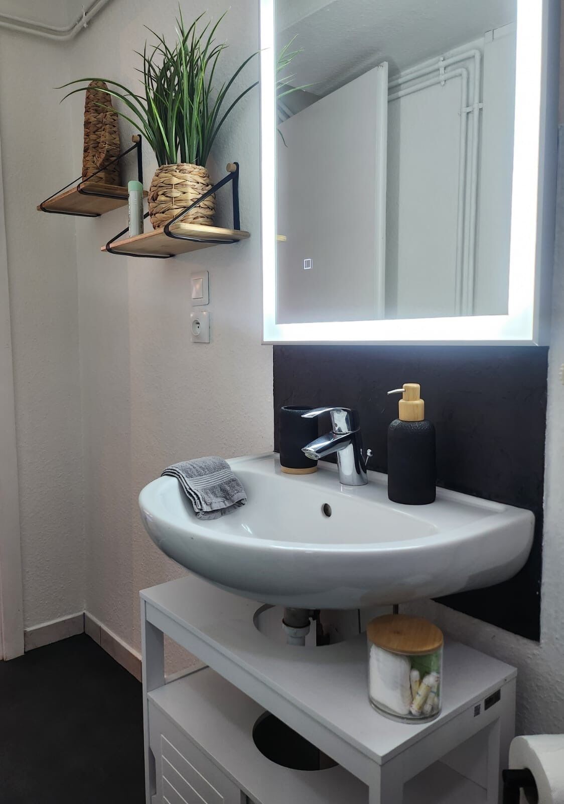 Une salle de bain avec un lavabo blanc, un miroir, une serviette et une étagère sur laquelle est posée une plante.