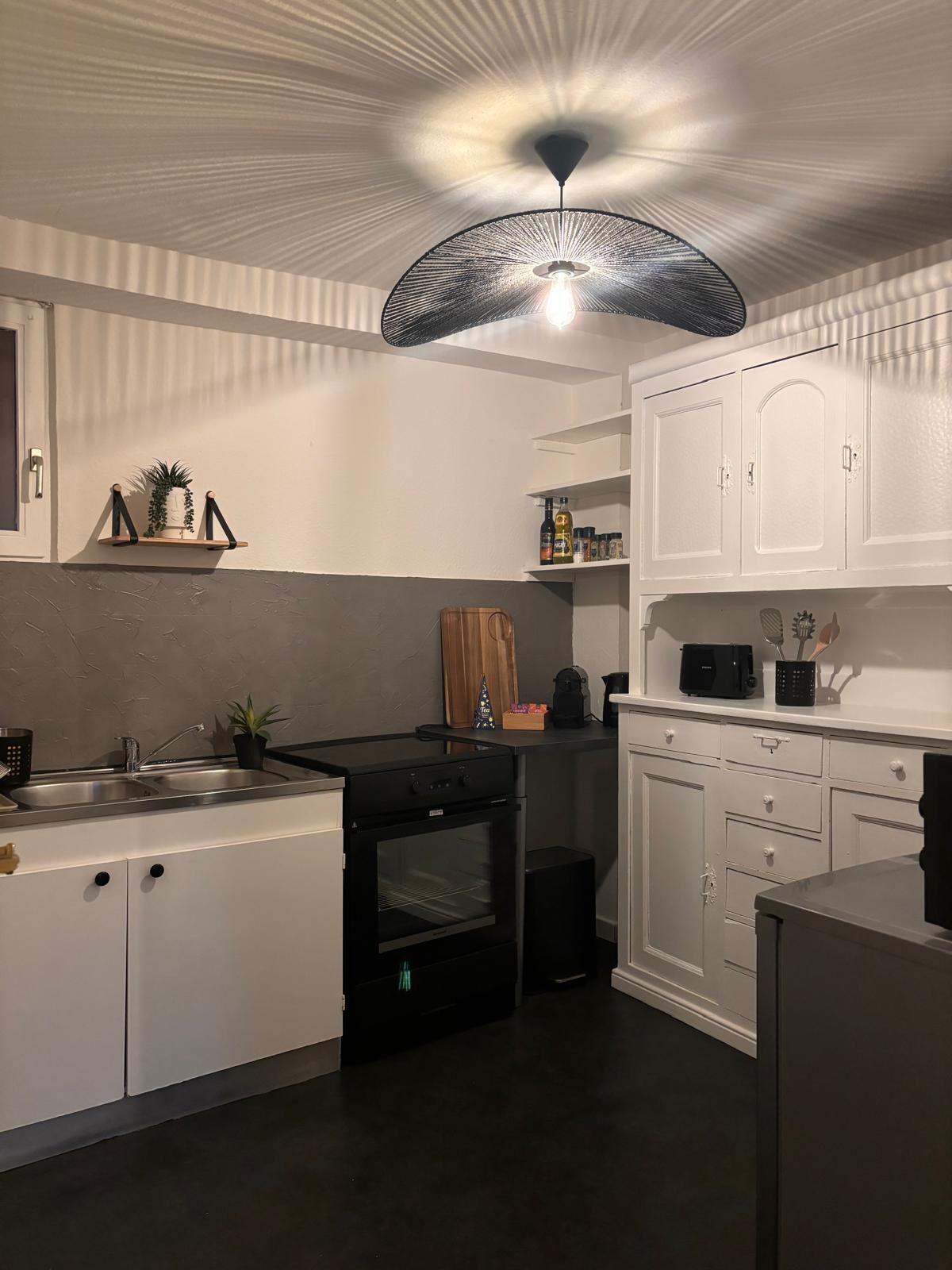 Una cocina moderna con armarios blancos, una estufa negra y una lámpara de techo original.