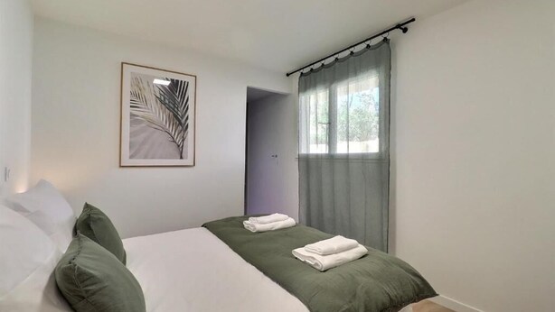 A bedroom with a bed, pillows, a green blanket, a framed picture on the wall, and a window with curtains. - Villa Altinea (Ventabren)