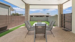 A covered patio with a table and chairs, a ceiling fan, and a view of a house in the background. - Zen Courtyard Garden - Patio - Garage (Darwin)