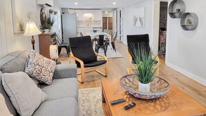 Un salon moderne avec un canapé gris, une table basse dotée d’un élément décoratif en verre, et un coin repas à l’arrière-plan.
