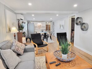 Ein modernes Wohnzimmer mit einem grauen Sofa, einem Couchtisch mit Glasdekor und einem Essbereich im Hintergrund.