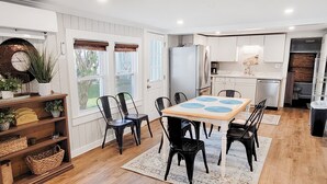 Une cuisine moderne avec des meubles blancs, un îlot central doté de tabourets et un coin repas avec une table et des chaises.