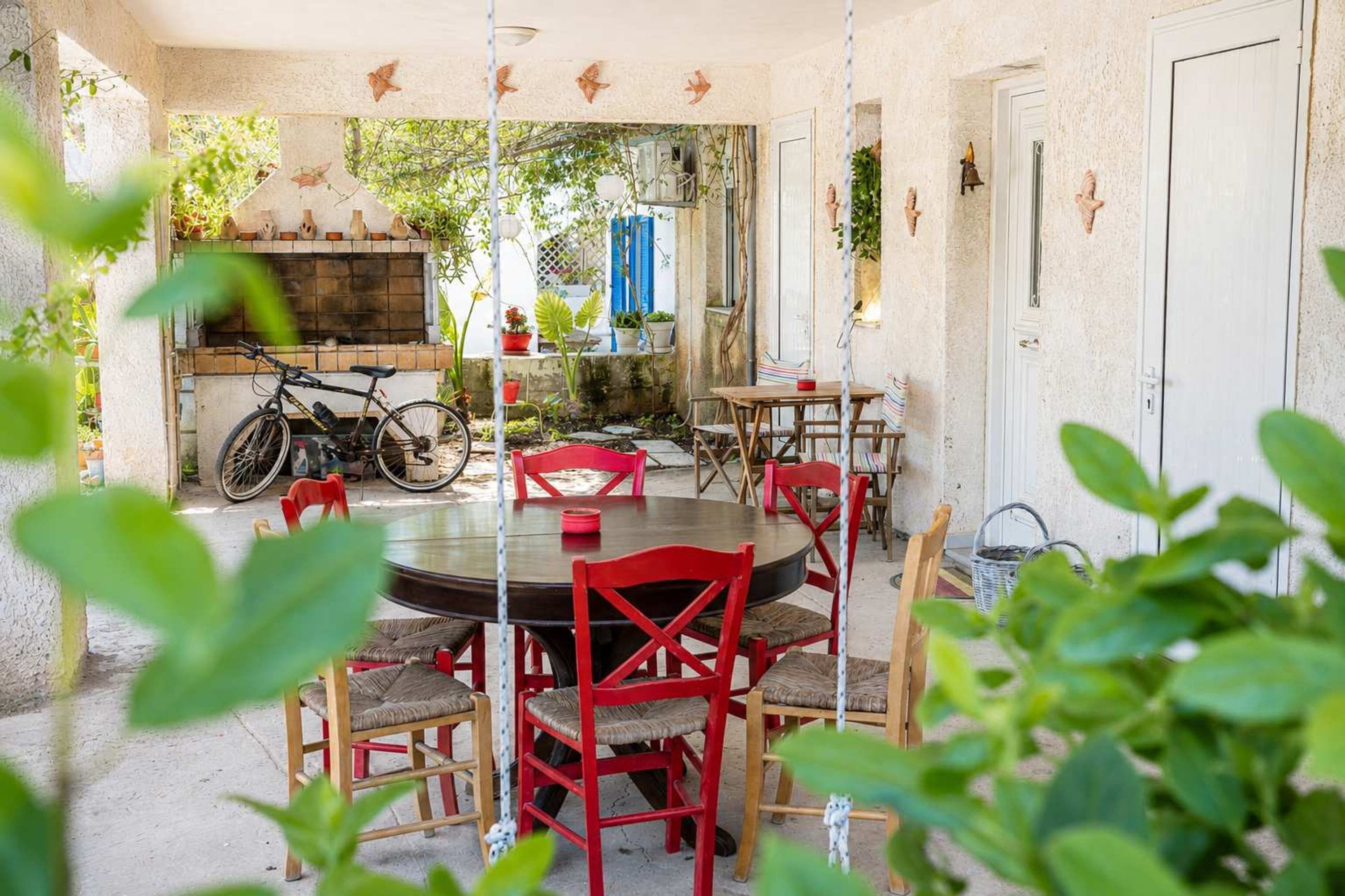 Un patio con un tavolo rotondo e sedie rosse, una bicicletta e un forno a mattoni.